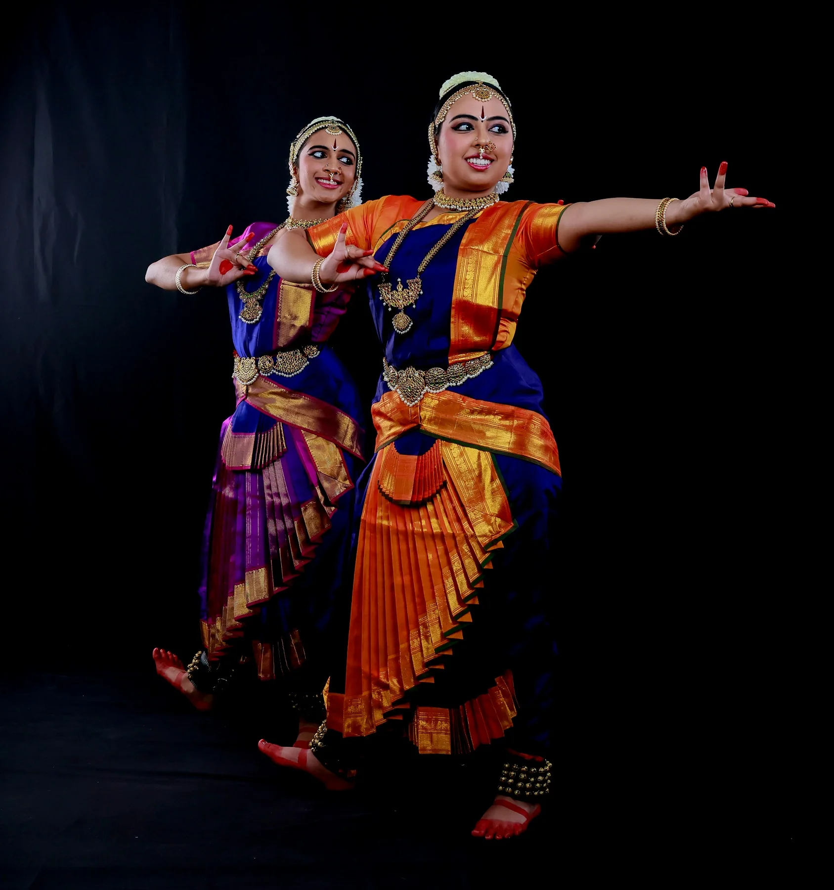 Shreya and Shriya in a high-energy action pose with open arms for the Varnam